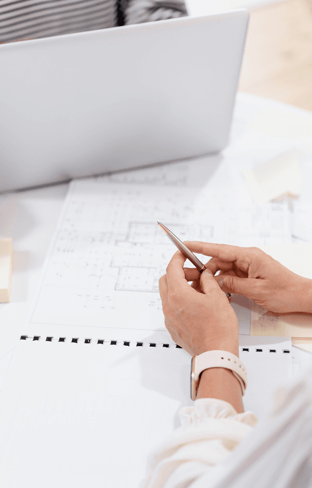 Beraterin notiert an Bauplänen am Schreibtisch – hochformatige Detailaufnahme